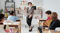 Junge Lehrerin steht vor einer Grundschulklasse und lächelt in die Kamera.