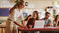 Lehrerin und Schülerin vor einem Laptop sprechen im Unterricht miteinander.