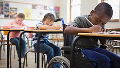 Ein Kind sitzt im Rollstuhl in einem Klassenraum mit anderen Kindern.