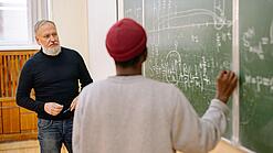 Ein Lehrer und ein Oberstufenschüler stehen vor einer Tafel.