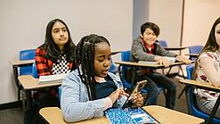 Junges Mädchen in einem Klassenraum schaut auf ihr Smartphone.