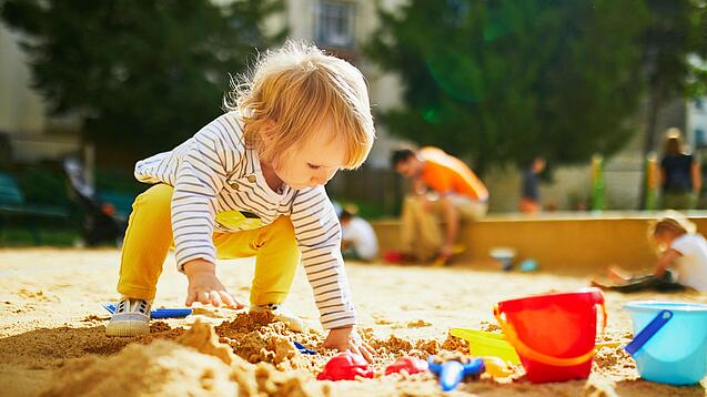 Kleines Kind spielt im Sandkasten mit Förmchen.