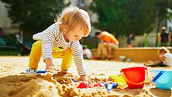 Kleines Kind spielt im Sandkasten mit Förmchen.