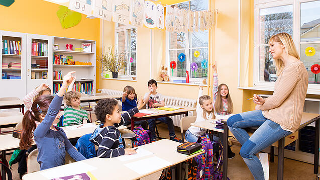 Grundschulkinder sitzen in einem Klassenraum und hören einer Lehrerin zu.