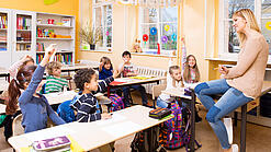 Grundschulkinder sitzen in einem Klassenraum und hören einer Lehrerin zu.