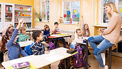Grundschulkinder sitzen in einem Klassenraum und hören einer Lehrerin zu.