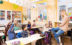 Grundschulkinder sitzen in einem Klassenraum und hören einer Lehrerin zu.