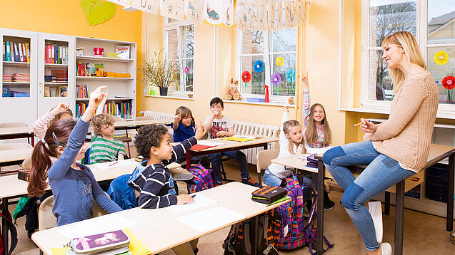 Grundschulkinder sitzen in einem Klassenraum und hören einer Lehrerin zu.