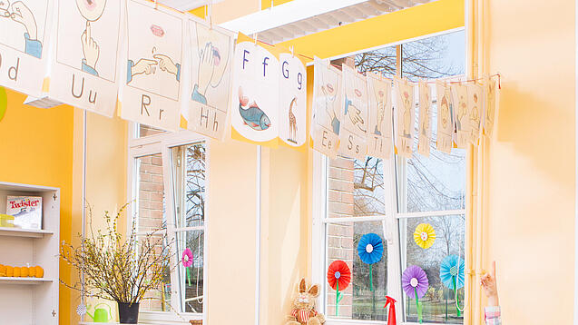 Grundschulkinder sitzen in einem Klassenraum und hören einer Lehrerin zu.