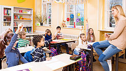 Grundschulkinder sitzen in einem Klassenraum und hören einer Lehrerin zu.