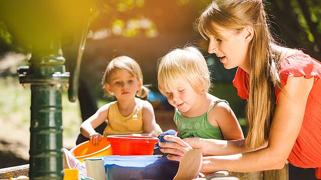 Eine pädagogische Fachkraft spielt mit Kindern im Garten.
