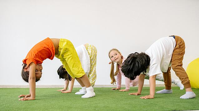 Drei Kleinkinder turnen auf einer grünen Matte.