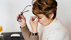 Erschöpfte Frau greift sich an die Nasenwurzel.