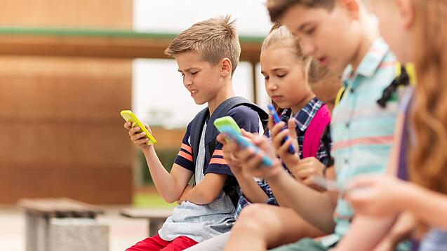 Kinder spielen auf dem Pausenhof am Handy.
