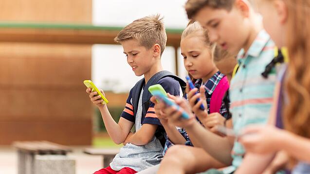 Kinder spielen auf dem Pausenhof am Handy.