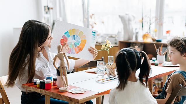 Junge Lehrerin zeigt zwei Kindern einen Farbkreis