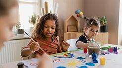 Zwei Kinder und eine junge Frau malen etwas.