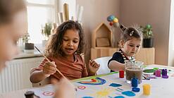 Zwei Kinder und eine junge Frau malen etwas.
