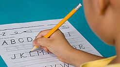 Ein Grundschulkind übt das Alphabet zu schreiben.