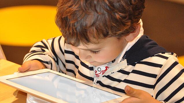 Ein kleines Kind schaut auf ein Tablet.