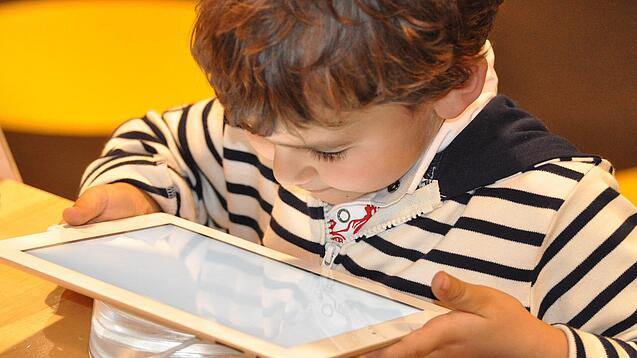 Ein kleines Kind schaut auf ein Tablet.