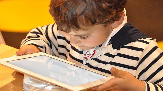 Ein kleines Kind schaut auf ein Tablet.