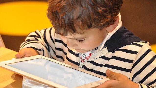 Ein kleines Kind schaut auf ein Tablet.