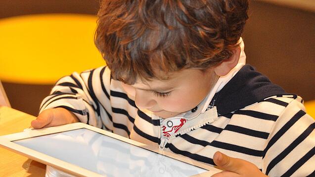 Ein kleines Kind schaut auf ein Tablet.