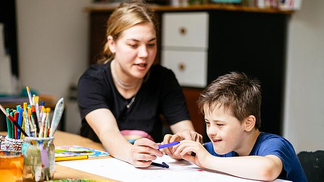 Junge mit besonderem Förderbedarf und eine Betreuerin an einem Tisch.