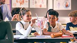 Zwei Kinder sitzen an einem Schultisch und haben ein Modell einer Windkraftturbine vor sich.