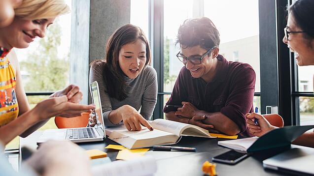 Gruppe junger Menschen sitzt gemeinsam an einem Tisch vor aufgeschlagenen Büchern.