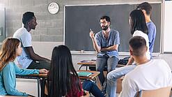 Gruppe diverser Schüler und Schülerinnen sitzt in einem Stuhlkreis und diskutiert mit einem Lehrer