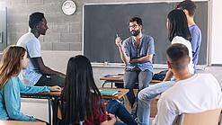 Gruppe diverser Schüler und Schülerinnen sitzt in einem Stuhlkreis und diskutiert mit einem Lehrer