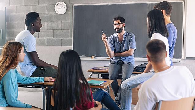 Gruppe diverser Schüler und Schülerinnen sitzt in einem Stuhlkreis und diskutiert mit einem Lehrer