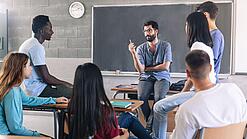 Gruppe diverser Schüler und Schülerinnen sitzt in einem Stuhlkreis und diskutiert mit einem Lehrer