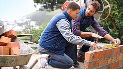 Zwei Männer bauen eine Mauer.