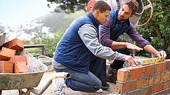 Zwei Männer bauen eine Mauer.