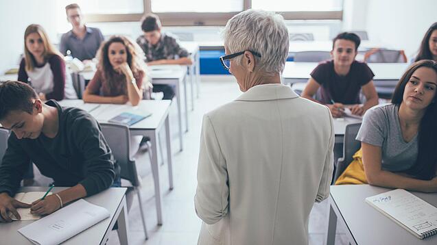 Eine Lehrerin steht vor einer Klasse von Oberstufenschülerinnen.