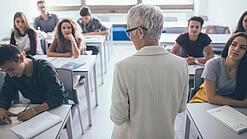 Eine Lehrerin steht vor einer Klasse von Oberstufenschülerinnen.