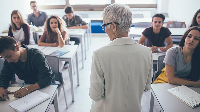 Eine Lehrerin steht vor einer Klasse von Oberstufenschülerinnen.
