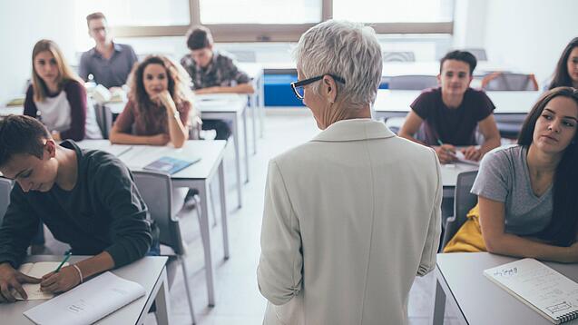 Eine Lehrerin steht vor einer Klasse von Oberstufenschülerinnen.