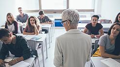 Eine Lehrerin steht vor einer Klasse von Oberstufenschülerinnen.