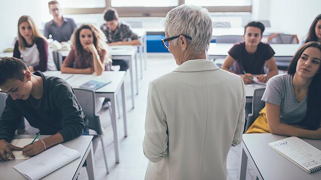 Eine Lehrerin steht vor einer Klasse von Oberstufenschülerinnen.