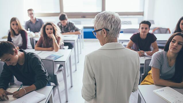 Eine Lehrerin steht vor einer Klasse von Oberstufenschülerinnen.