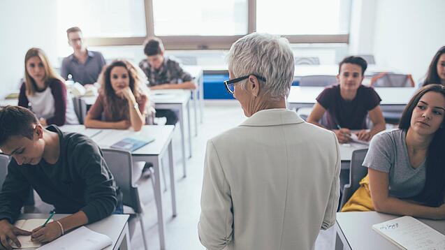 Eine Lehrerin steht vor einer Klasse von Oberstufenschülerinnen.