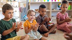 Kindergartenkinder sitzen in einem Kreis und klatschen in die Hände.