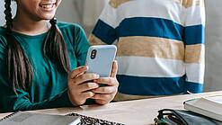 Zwei Kinder mit einem Smartphone an einem Schreibtisch.