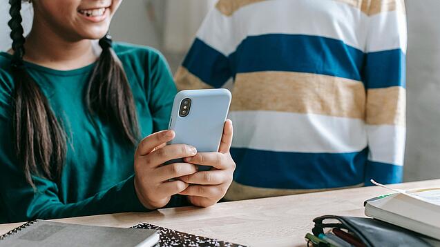 Zwei Kinder mit einem Smartphone an einem Schreibtisch.