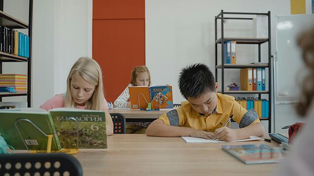 Drei Schulkinder arbeiten in einem Klassenraum an ihren Schreibtischen.