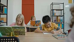 Drei Schulkinder arbeiten in einem Klassenraum an ihren Schreibtischen.